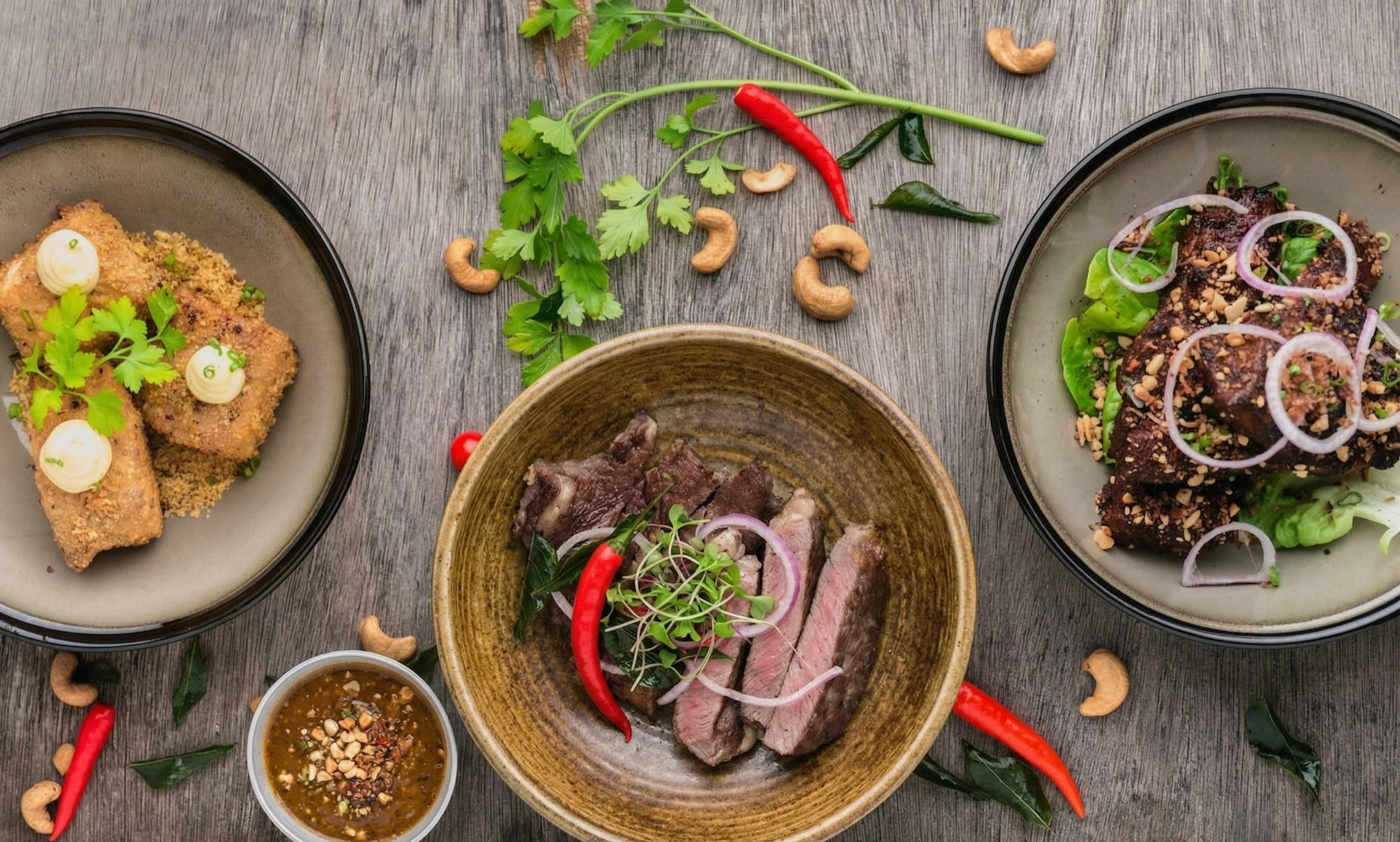 Drei angerichtete Teller mit Fleischgerichten auf einem Holztisch